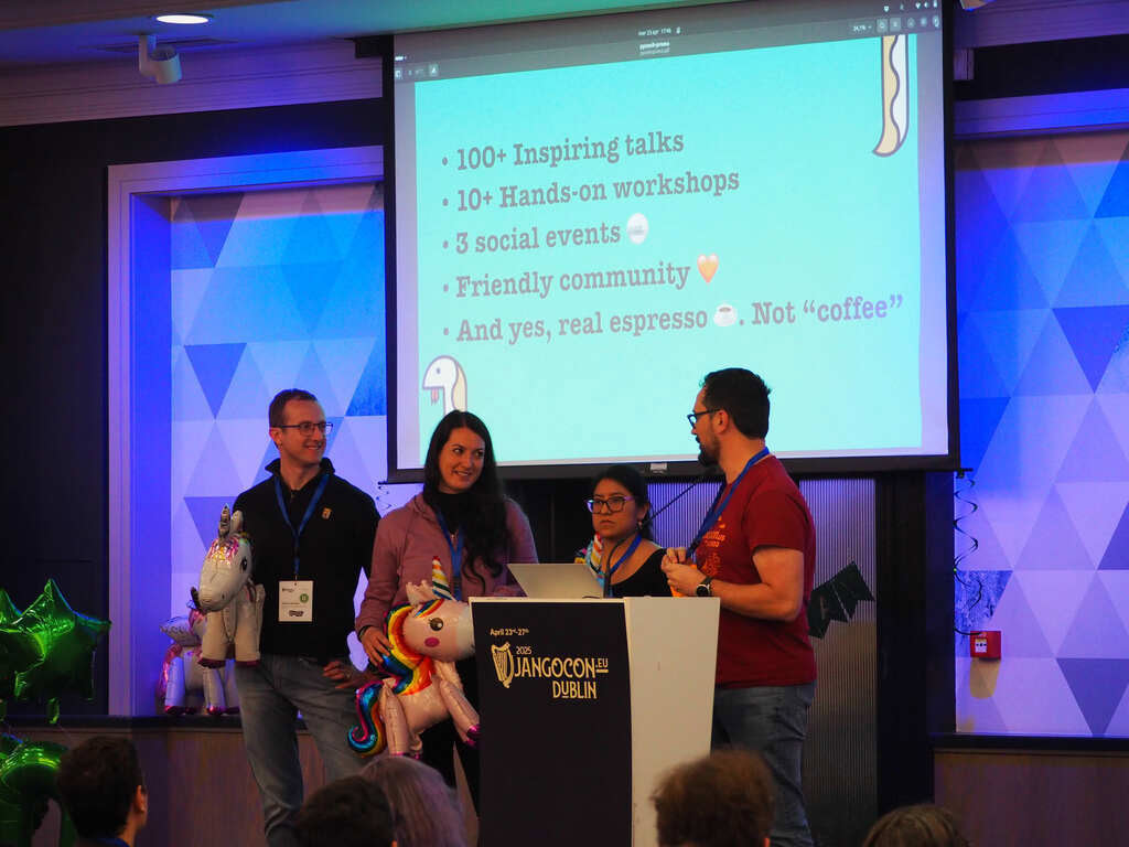 Four people on stage, presenting PyCon Italia 2025 in a lightining talk, holding inflatable pony balloons
