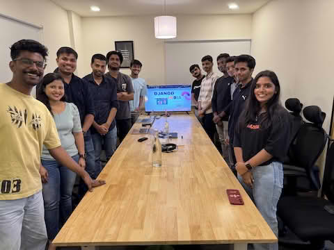 Django India meetup participants smiling at the camera, standing around a table in a conference room