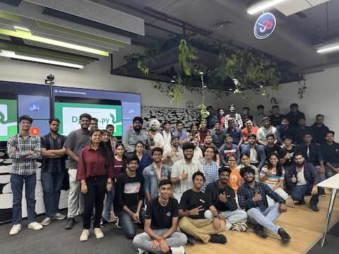 Full room of attendees for Django India X PyDelhi meetup, they are all looking at the camera, smiling, thumbs up and V hand signs