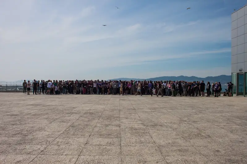 Group photo of conference attendees, on a large patio, with the sea and coastline visible in the background