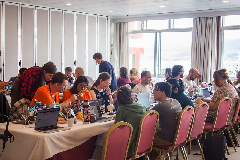 Conference sprint attendees sitting around a table, working on their laptops and chatting to each other