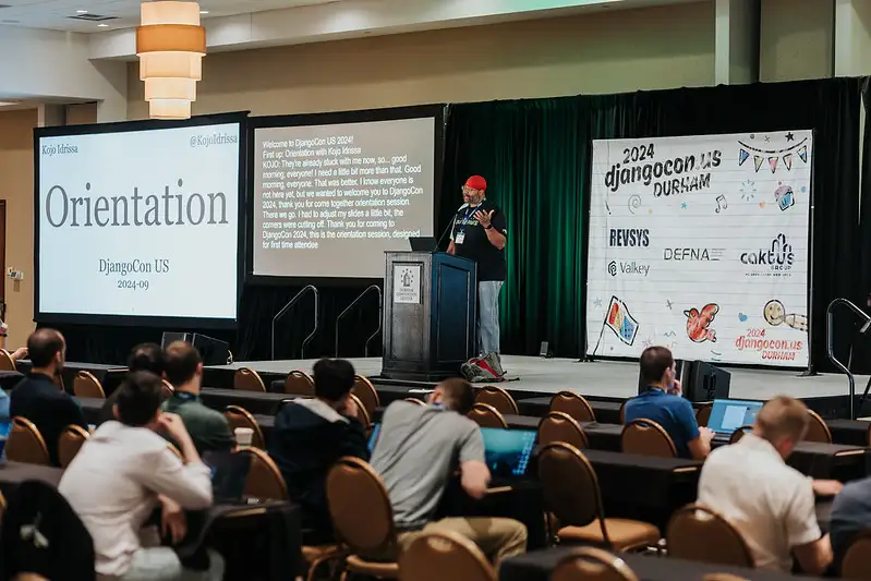 Kojo Idrissa on the stage at DjangoCon US 2024, with a slide reading 'Orientation' DjangoCon US 2024-09