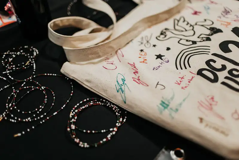 Close-up picture of a DjangoCon US 2024 tote bag on a table, which has been signed multiple times in many different colors