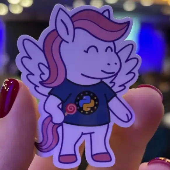 Close-up of a Django pony sticker someone is holding. The pony is smiling and wears a EuroPython Society shirt