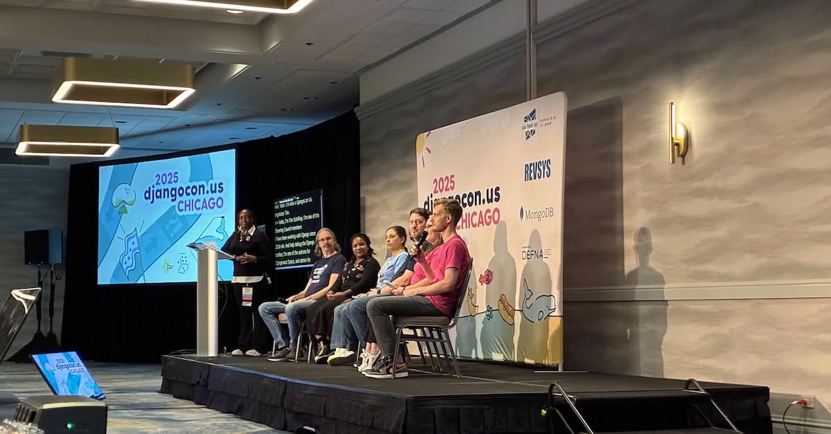 One host and six panelists on stage at DjangoCon US 2025 in Chicago. Host Velda Kiara stands next to the podium. Panelists are seated: Peter Grandstaff, Dawn Wages, Natalia Bidart, Jeff Triplett, Rachell Calhoun, Tim Schilling holding the microphone